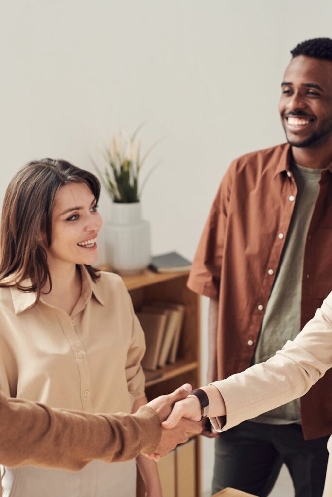 Four colleagues smiling and shaking hands in a bright office setting.